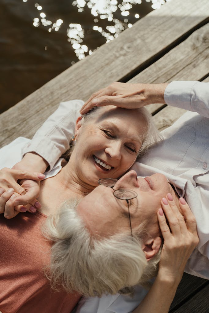 Elderly couple enjoying a sunny day on a wooden dock by the water, sharing a tender moment.