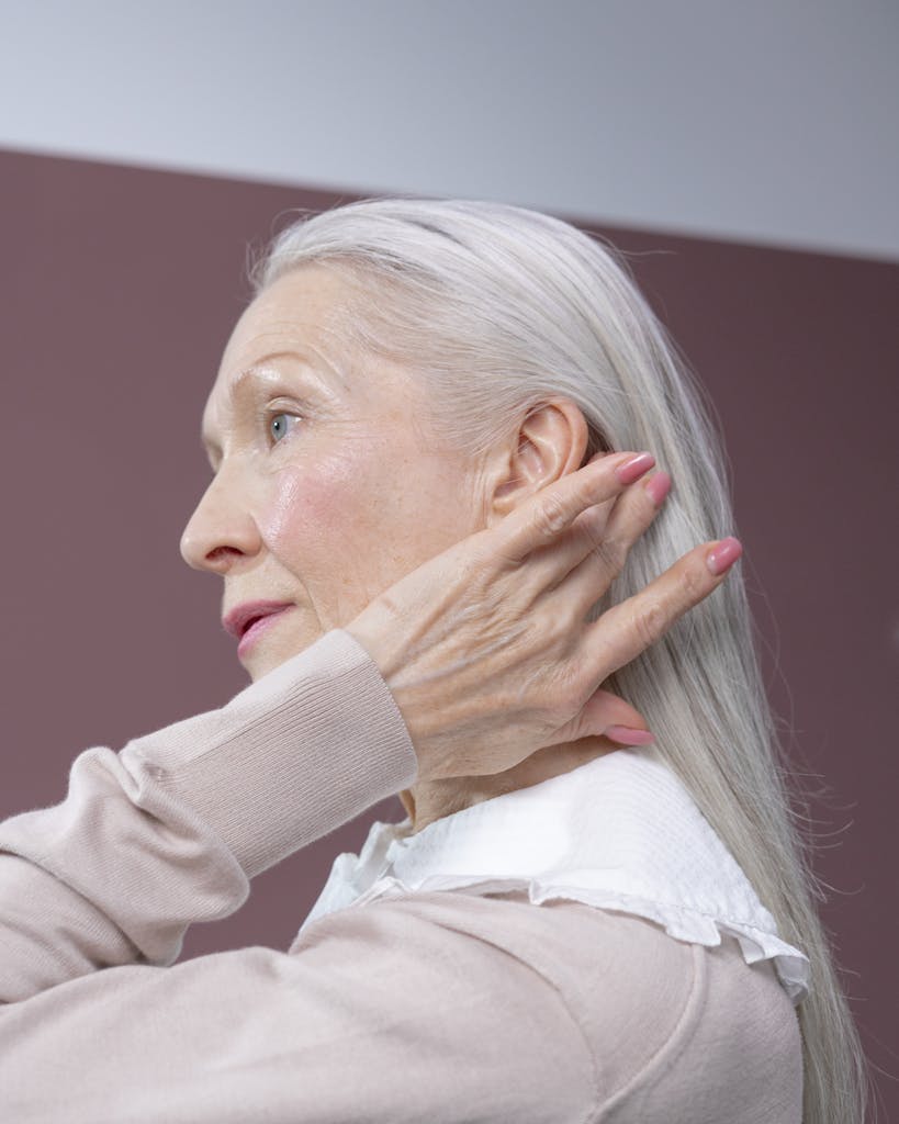 Profile of a senior woman with long grey hair, touching her hair in a serene pose.