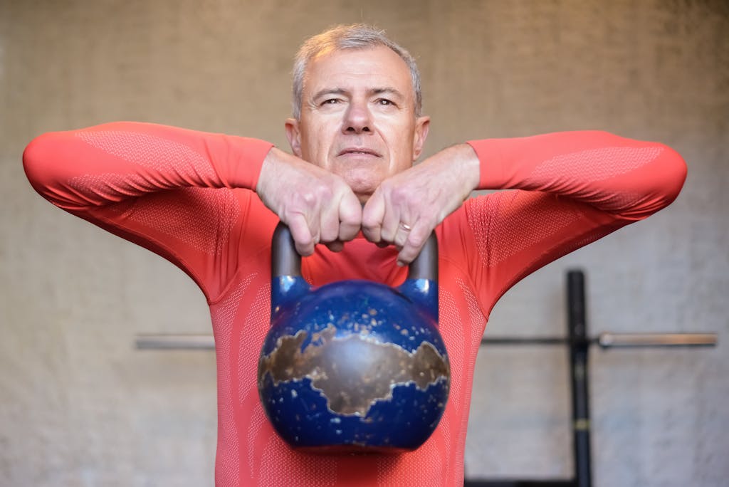 Senior man performing kettlebell exercises indoors, showcasing strength and healthy living.